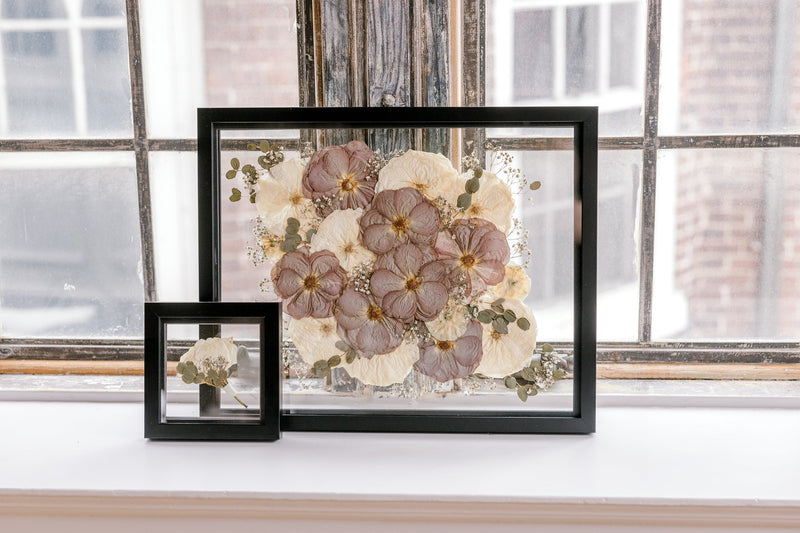Two black frames showcase preserved wedding flowers pressed in between two panes of glass. 