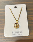 A pressed flower necklace with a tiny white flower is set in a circular gold-plated bezel cup. It is placed atop a wooden surface. 