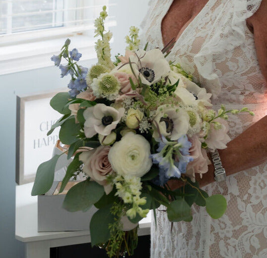 A bridal bouquet held by her bride with white, mauve, blue flowers. 