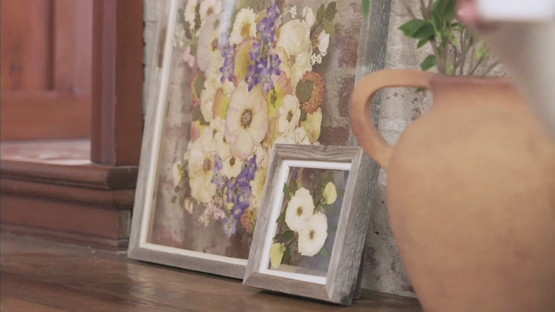 Pressed bouquet art sits on a bench leaning against a brick wall. These pressed flower frames are made of barn wood and showcase colorful flowers pressed by the Pressed Bouquet Shop.