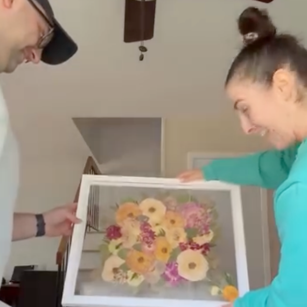 A couple unboxes their bouquet preservation from Element Design, showing their pressed flower frame with brightly colored blooms. 