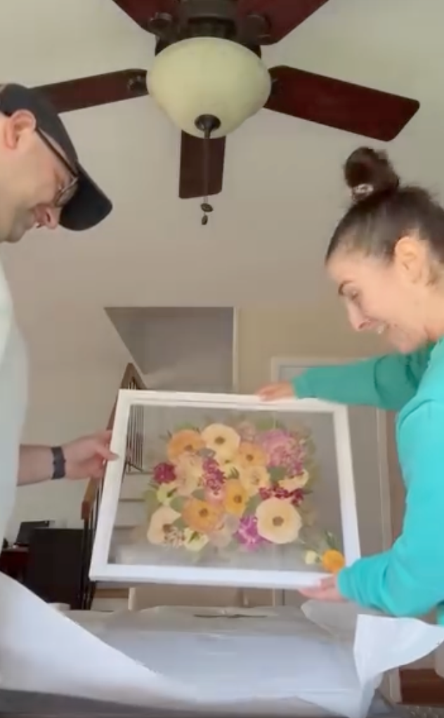 A couple unboxes their bouquet preservation from Element Design, showing their pressed flower frame with brightly colored blooms. 