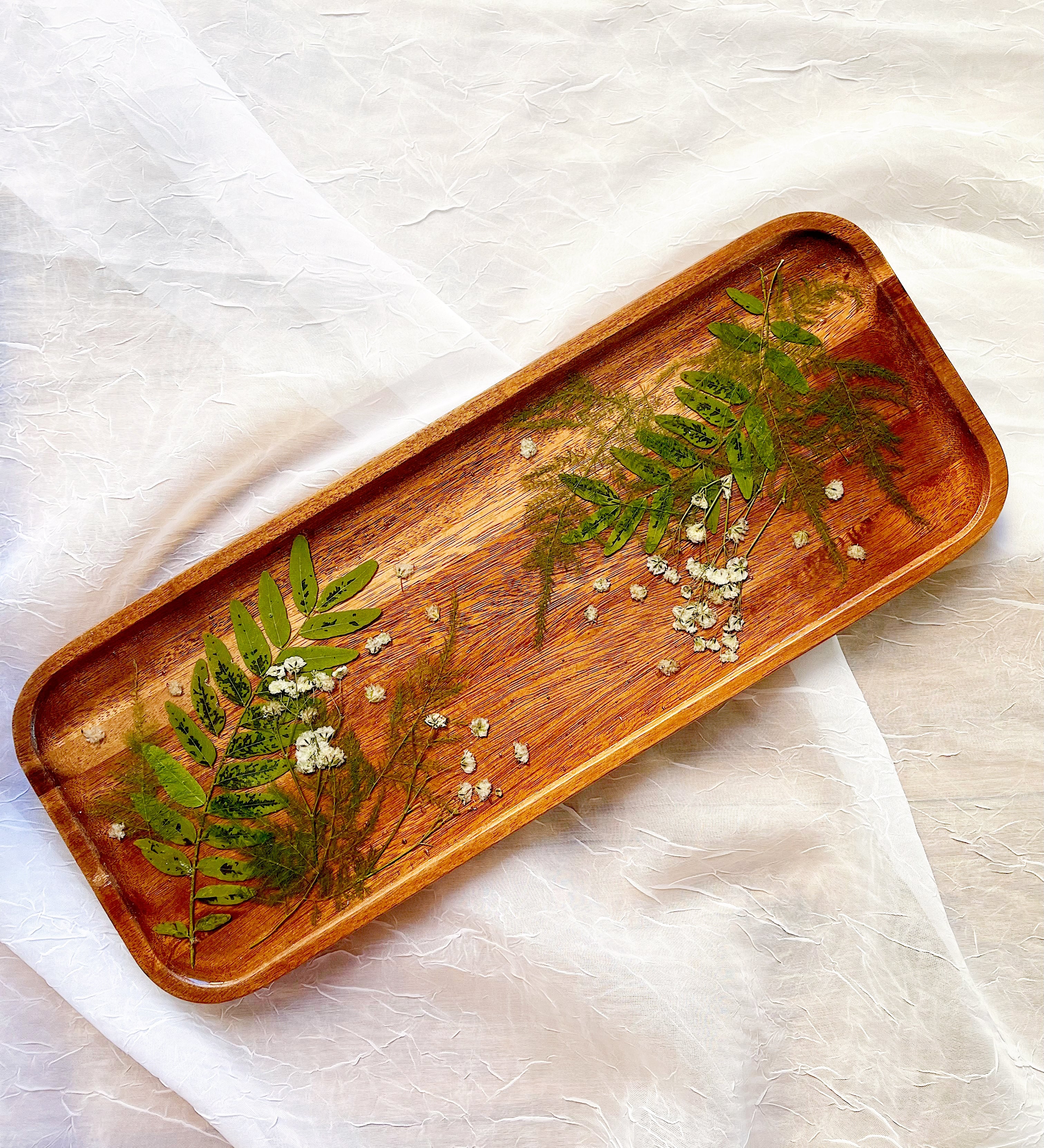 Pressed greenery and baby's breath on a wooden resin tray for home decor