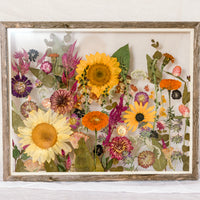 A bright arrangement of pressed sunflowers and wildflowers displayed inside of a barn wood floating frame.