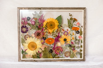 A bright arrangement of pressed sunflowers and wildflowers displayed inside of a barn wood floating frame.