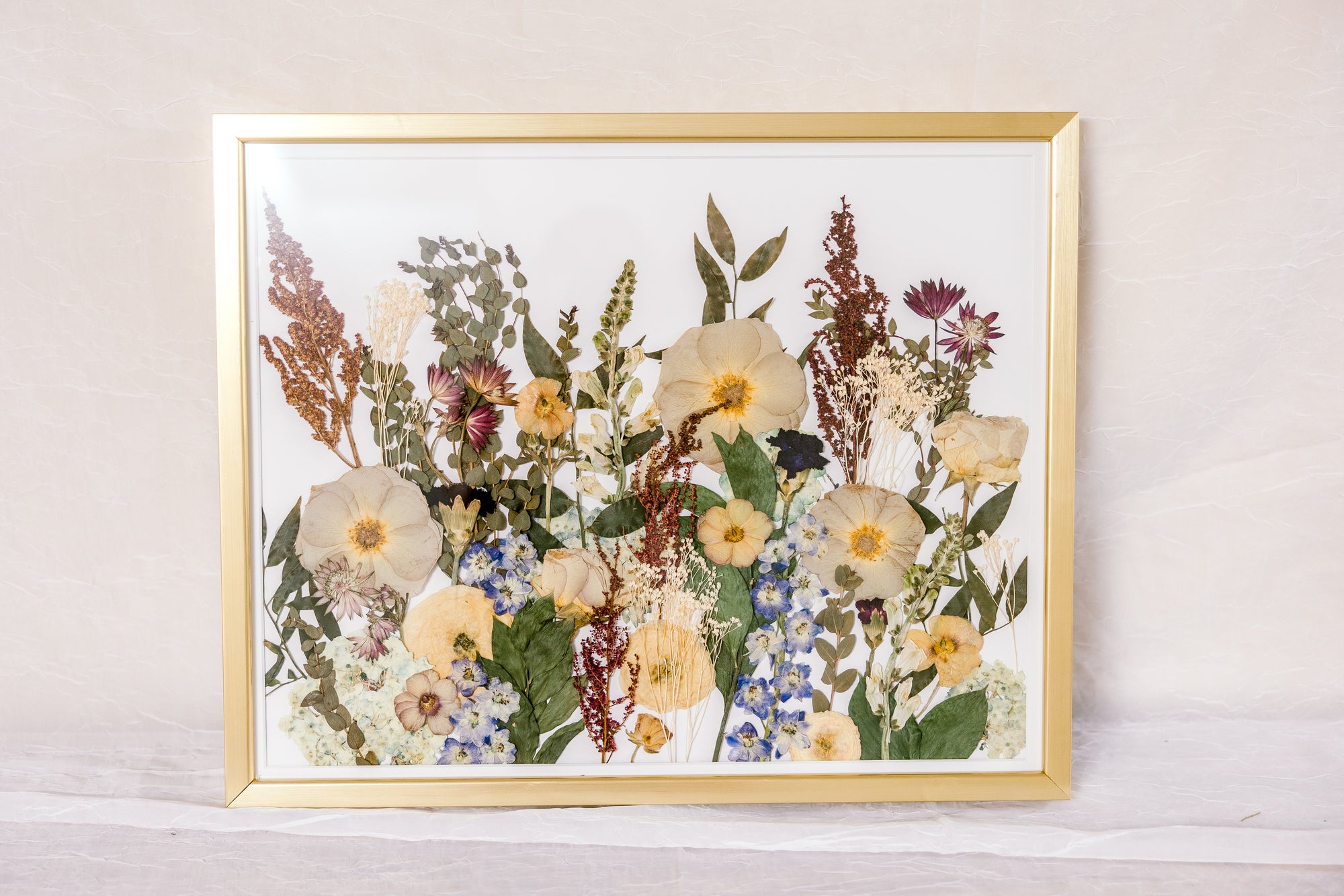 A collection of pressed flowers &quot;grow&quot; up from the bottom of this gold wood frame to appear as if they have grown from a field. 