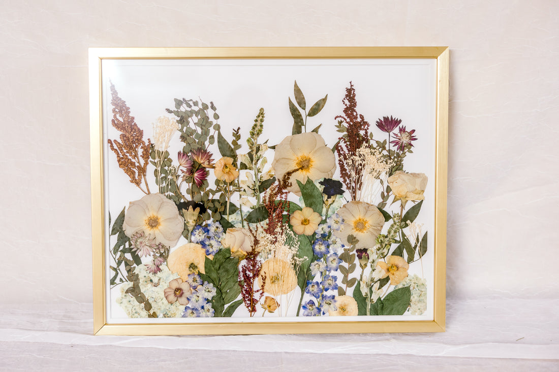 A collection of pressed flowers "grow" up from the bottom of this gold wood frame to appear as if they have grown from a field. 