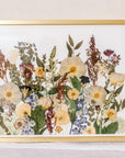 A collection of pressed flowers "grow" up from the bottom of this gold wood frame to appear as if they have grown from a field. 