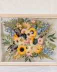 A wildflower wedding bouquet pressed and framed inside a natural wood frame.