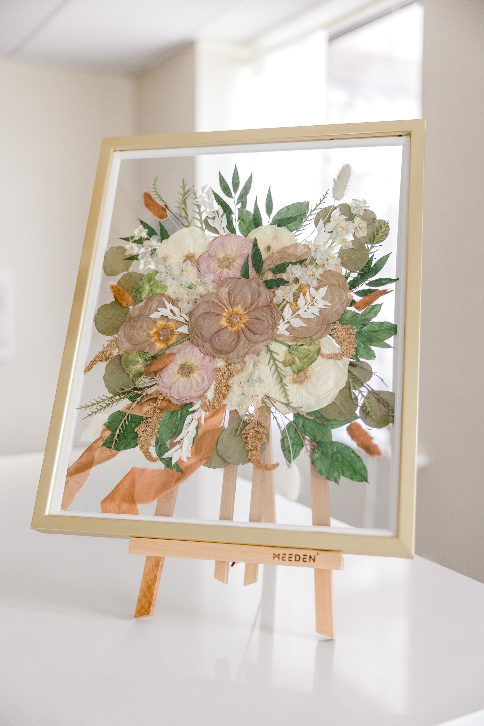 A gold wood frame with pressed flowers from a bridal bouquet, detailed by the ribbon that surrounded the wedding flower stems. 