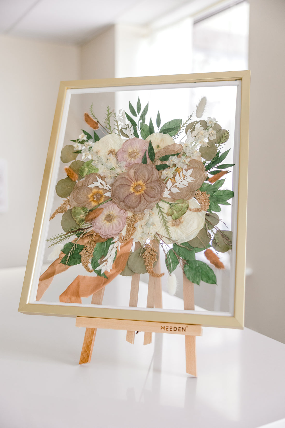 A gold wood frame with pressed flowers from a bridal bouquet, detailed by the ribbon that surrounded the wedding flower stems. 