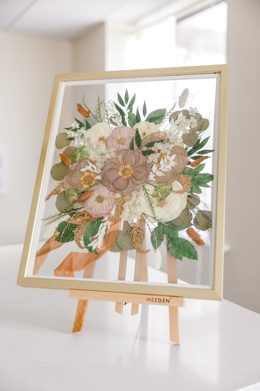 A gold wood frame with pressed flowers from a bridal bouquet, detailed by the ribbon that surrounded the wedding flower stems. 