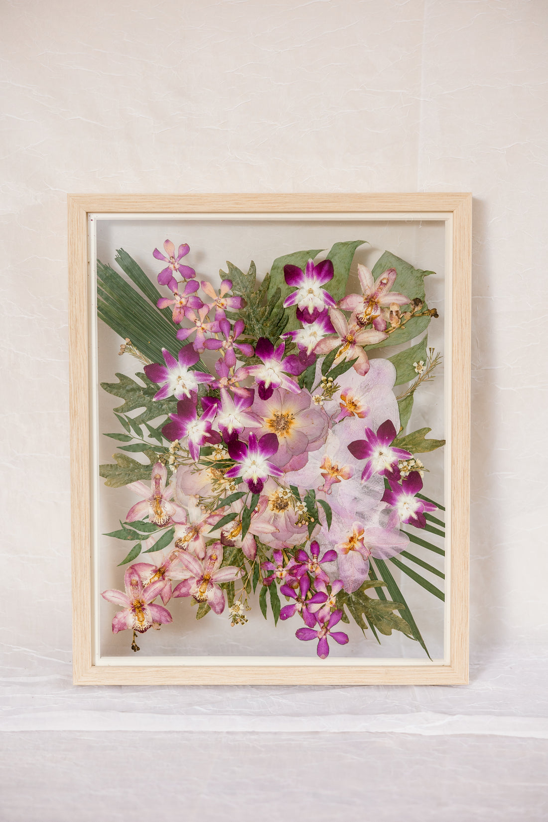 A bright and vibrant pink and green bouquet made up of orchids and roses has been pressed and framed in a natural wood bouquet preservation frame.